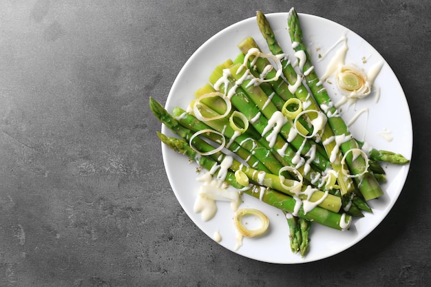 Photo healthy asparagus dish with sliced onion on white plate against grey background