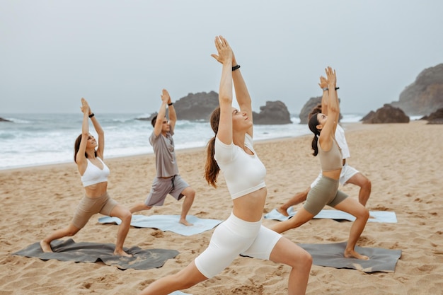 Healthy balance lifestyle yoga class at ocean beach in the morning doing warrior poses with calm