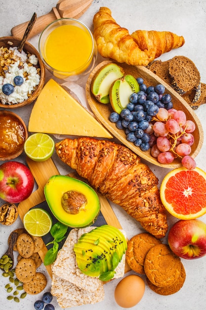 Healthy balanced breakfast on white background. Muesli, juice, croissants, cheese, biscuits and fruit, top view.