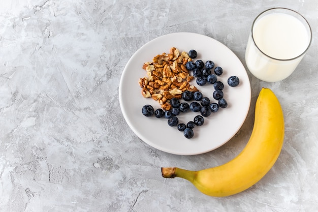 Healthy breakfast, blueberry, walnut, banana, glass of milk on cement