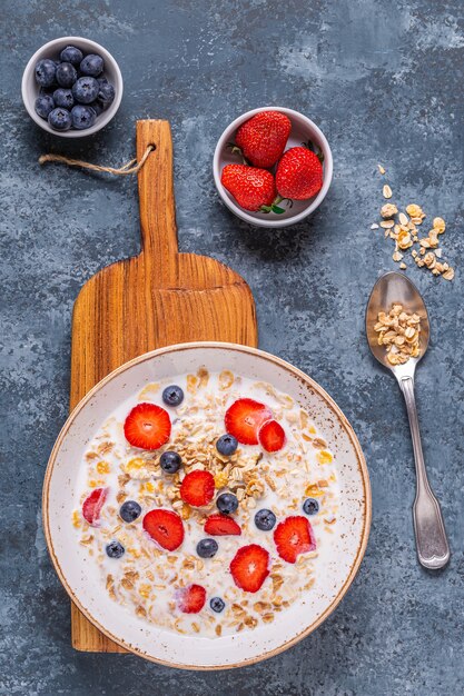 Healthy breakfast, bowl with oat granola, milk and berries, top view.