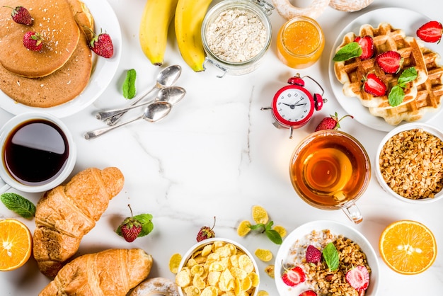 Healthy breakfast eating concept, various morning food - pancakes, waffles, croissant oatmeal sandwich and granola with yogurt, fruit, berries, coffee, tea, orange juice, white background