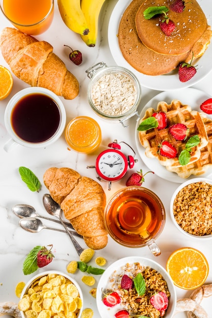 Healthy breakfast eating concept, various morning food - pancakes, waffles, croissant oatmeal sandwich and granola with yogurt, fruit, berries, coffee, tea, orange juice, white background