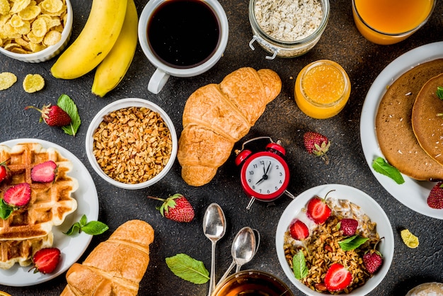 Healthy breakfast eating concept, various morning food - pancakes, waffles, croissant oatmeal sandwich and granola with yogurt, fruit, berries, coffee, tea, orange juice