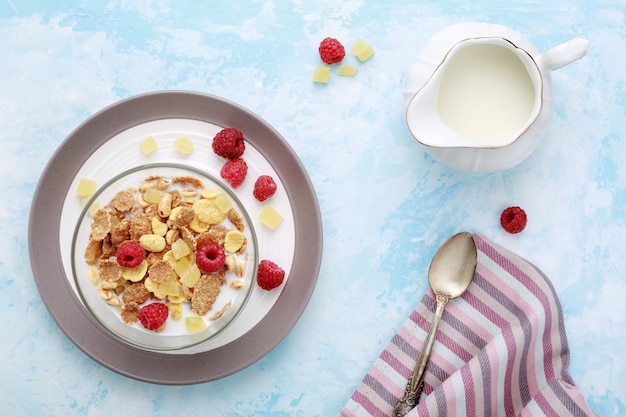 Healthy breakfast flakes with raspberries and milk on blue table