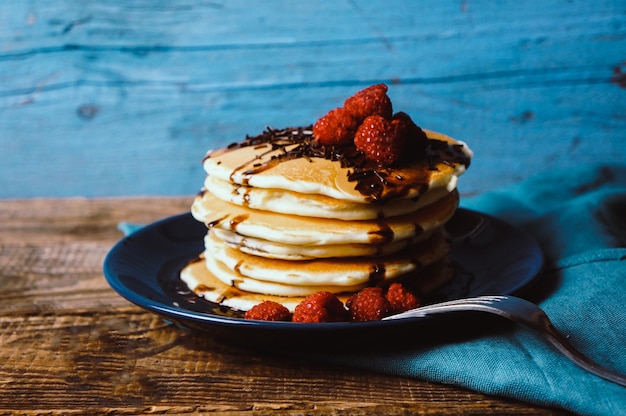 Healthy breakfast homemade pancakes with fresh raspberries and chocolate sauce on an old wooden table copy space