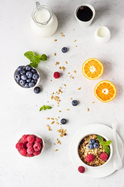 Healthy breakfast ingredients. Bowl of homemade granola with milk, fresh berries (blueberry and raspberry), orange and milk. 