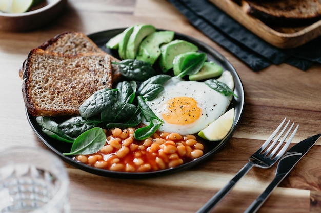 Healthy breakfast or lunch at home or cafe with fried egg avocado toasts beans and fresh spinach on a wooden table