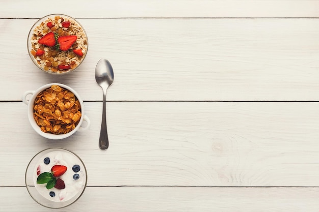 Healthy breakfast meals on wooden table copy space. Cornflakes, muesli and yogurt with berries and spoon, top view