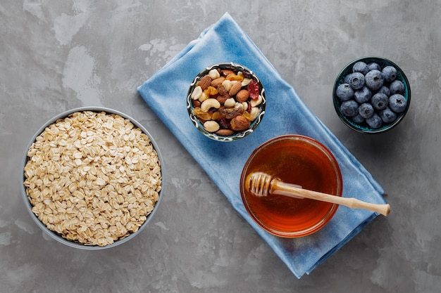 Healthy breakfast oatmeal with berries, nuts and honey. Oat flakes, blueberries, honey and assorted nuts on a gray background. Vegan breakfast with oatmeal. Top view