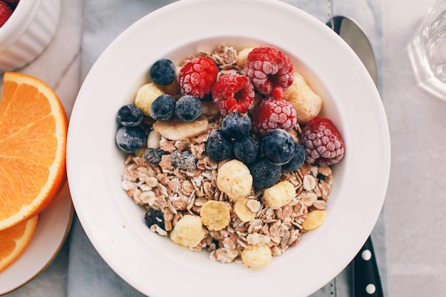 Healthy breakfast: oatmeal with  raspberries,oranges and blueberries. Homemade granola. Healthy breakfast ingredients. Bowl of oat granola with milk, fresh fruit. Top view, copy space