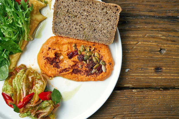 Photo healthy breakfast - omelet with kimchi and baked peppers hummus in a plate on a wooden