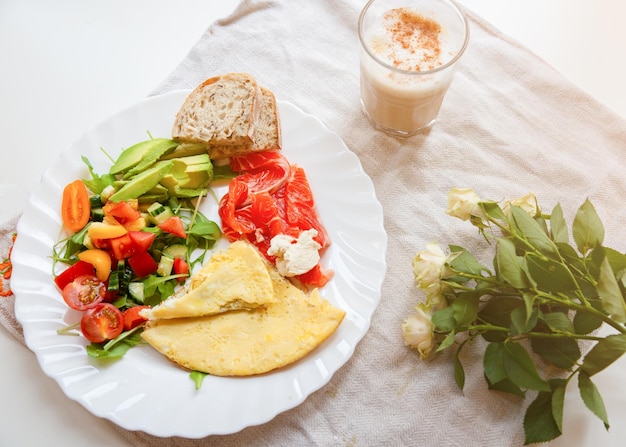 Healthy breakfast Omelette with tomatoes and rucola salad Salmon with wholemeal bread Cappuccino and roses on the rustic linen background Ideal morning flat lay