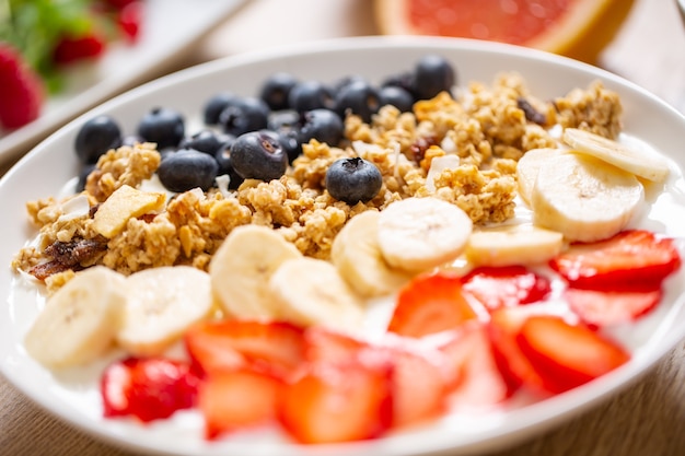 Healthy breakfast served with plate of yogurt muesli blueberries strawberries and banana. Morning table granola almonds berries citrus fruits juice and green herbs.