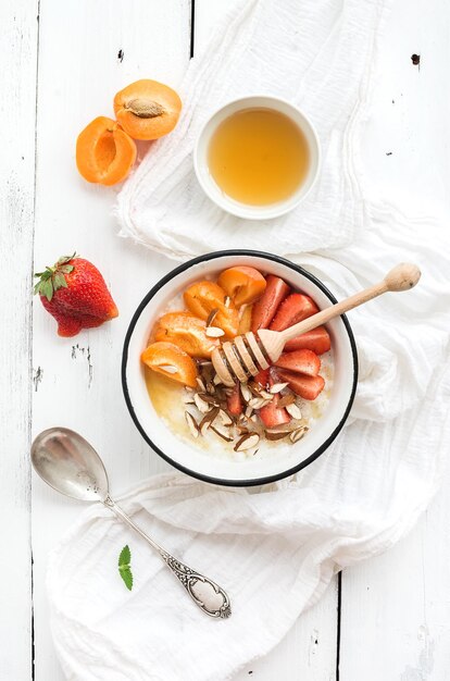 Healthy breakfast set Rice cereal or porridge with fresh strawberry apricots almond and honey over white rustic wood backdrop top view