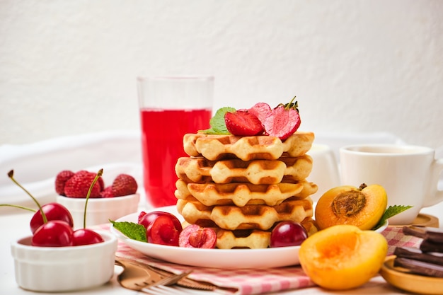 Healthy Breakfast set with Belgian waffles with strawberries, apricots, cherries, juice and a cup of black coffee and bitter chocolate on white stone table background