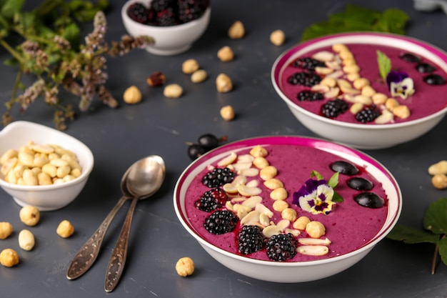 Healthy breakfast smoothie bowl with blackberries, gooseberries, peanuts, hazelnuts, decorated with flowers