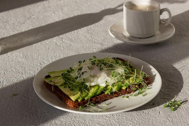 Healthy breakfast toasted whole grain bread with avocado poached egg microgreens and a cup of coffee