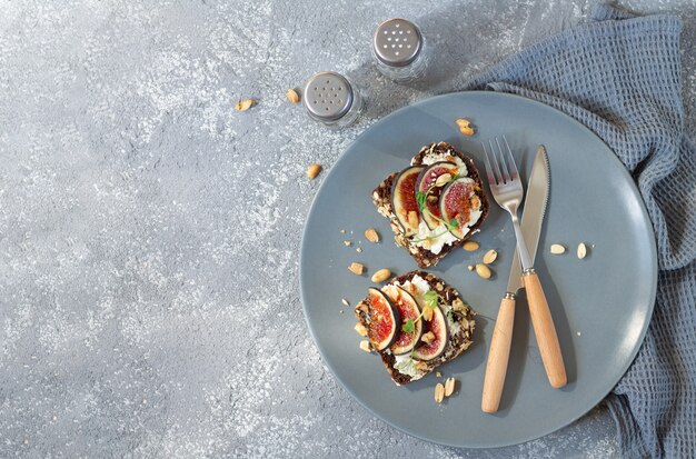 Healthy breakfast toasts with fresh figs, cream cheese, nuts and spices on plate top view