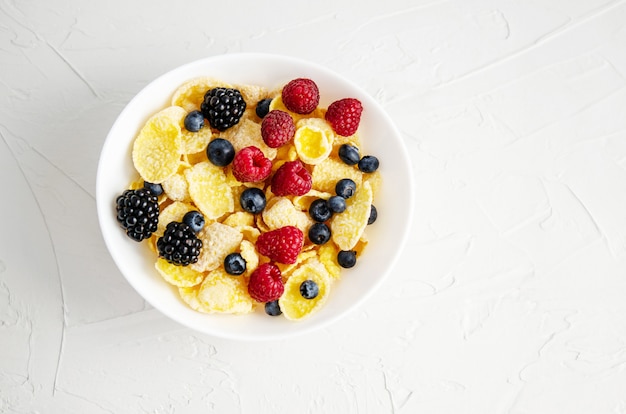 Healthy breakfast with cornflakes in a white plate, berries, milk and coffee.