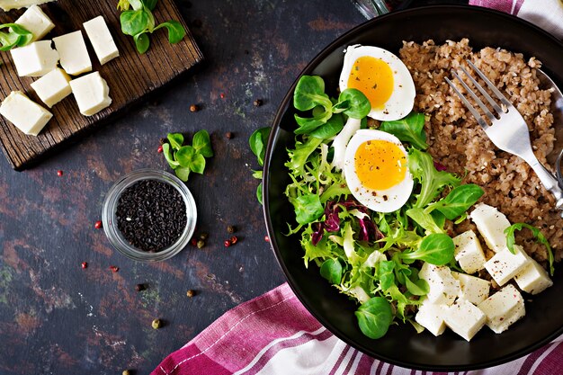 Healthy breakfast with egg, cheese, lettuce  and buckwheat porridge on dark. Dietary menu. Flat lay. Top view