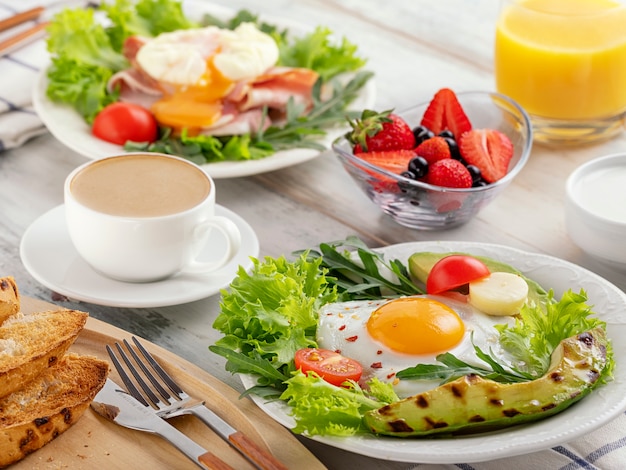 Healthy breakfast with fried eggs, avocado, tomato, toasts and coffee and orange juice.