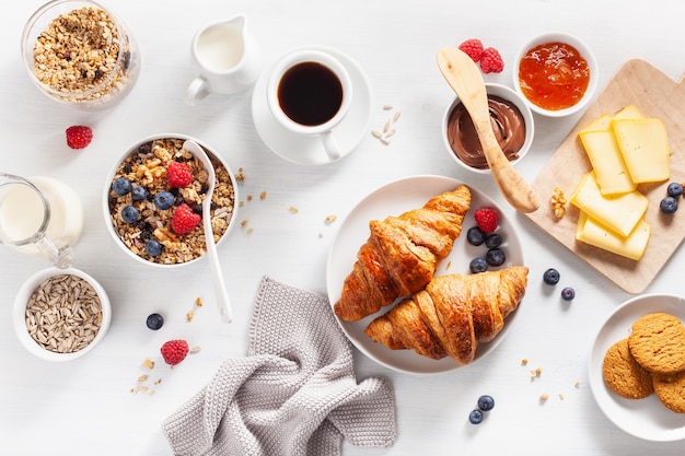 Healthy breakfast with granola, berry, nuts, croissant, jam, chocolate spread and coffee. Top view