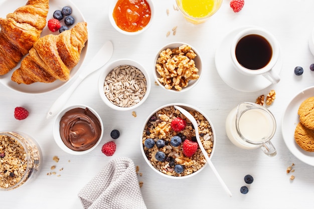 Healthy breakfast with granola, berry, nuts, croissant, jam, chocolate spread and coffee. Top view