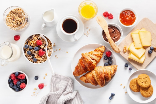 Healthy breakfast with granola, berry, nuts, croissant, jam, chocolate spread and coffee. Top view