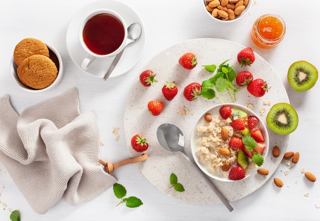 Healthy breakfast with oatmeal porridge, strawberry, nuts, jam and tea. Top view