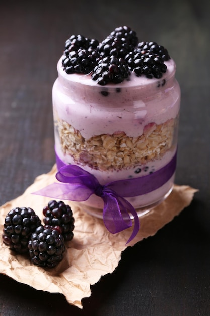 Healthy breakfast yogurt with blackberries and muesli served in glass jar on dark background