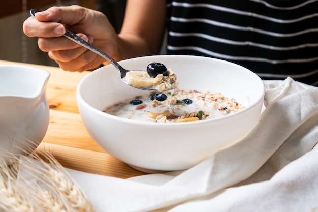 Healthy breakfast. Young Asian woman eating fresh granola, muesli with milk and berries on wooden table background.