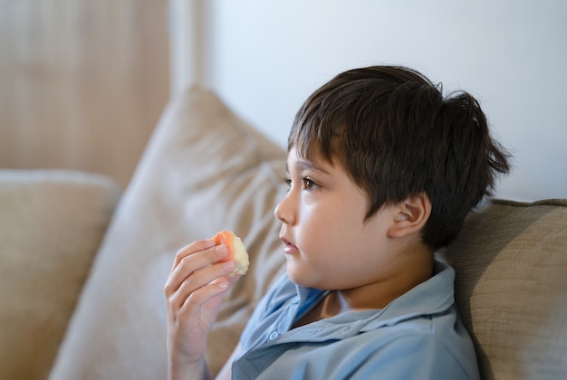 Healthy child eating red apple while watching TV, Cute boy eating fresh fruit for his snack, Close up kid face eating food. Healthy food for children concept