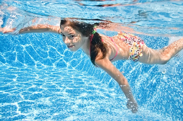 Healthy child swims underwater in swimming pool active little girl dives and has fun under water