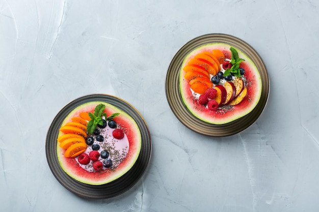 Healthy clean eating dieting and nutrition seasonal summer breakfast concept Fruit salad with yogurt in carved watermelon bowl on a kitchen table Top view flat lay copy space background