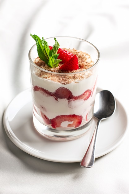 Healthy dessert in glass with fresh strawberries and cream yogurt on white background