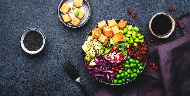 Healthy diet food Vegan buddha bowl with quinoa fried tofu avocado edamame beans peas radish red cabbage and sesame seeds Black kitchen table background top view banner