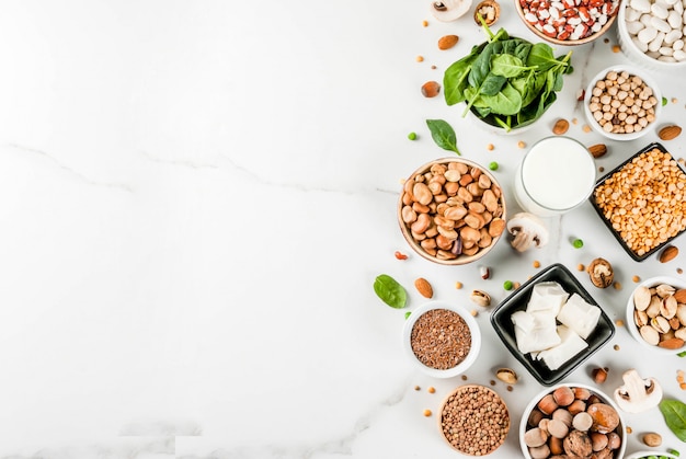 Healthy diet vegan food, veggie protein sources: Tofu, vegan milk, beans, lentils, nuts, soy milk, spinach and seeds. Top view on white table.