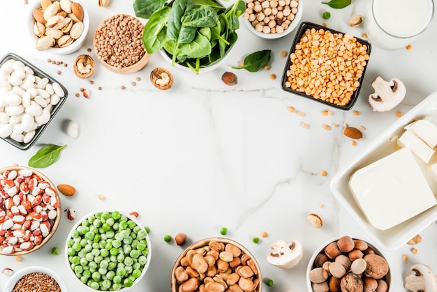 Healthy diet vegan food, veggie protein sources: Tofu, vegan milk, beans, lentils, nuts, soy milk, spinach and seeds. Top view on white table.