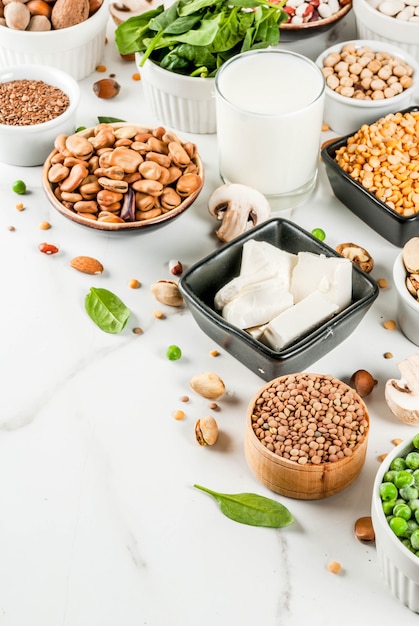 Healthy diet vegan food, veggie protein sources: Tofu, vegan milk, beans, lentils, nuts, soy milk, spinach and seeds. Top view on white table.