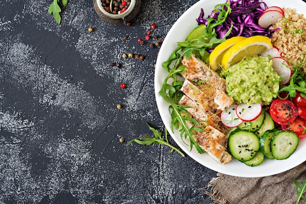 Healthy dinner. Buddha bowl lunch with grilled chicken and quinoa, tomato, guacamole, red cabbage, cucumber and arugula. Flat lay. Top view