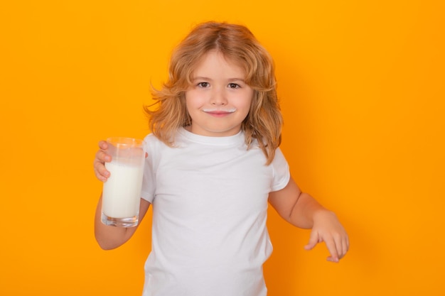 Healthy drink with calcium and protein for kids Child with a glass of milk on studio background Cute boy in white shirt holding glass of milk on isolated on yellow Kid with milk mustache