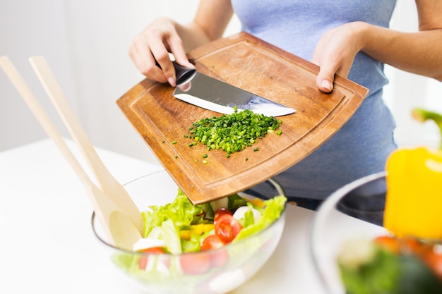 healthy eating, cooking, vegetarian food, diet and people concept - close up of woman adding chopped green onion to salad