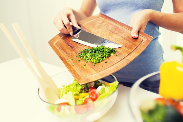 healthy eating, cooking, vegetarian food, diet and people concept - close up of woman adding chopped green onion to salad