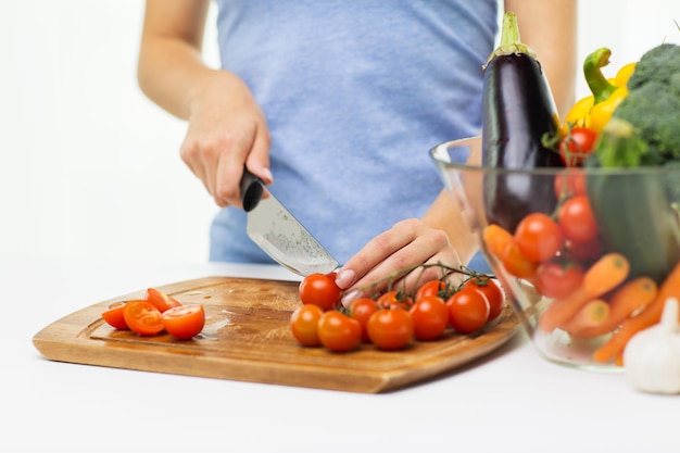 healthy eating, cooking, vegetarian food, dieting and people concept - close up of woman chopping tomatoes with knife on cutting board