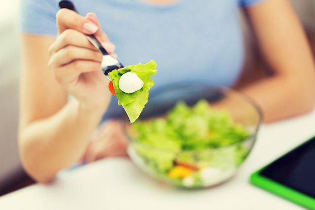 healthy eating, diet, food and people concept - close up of young woman eating vegetable salad with fork at home