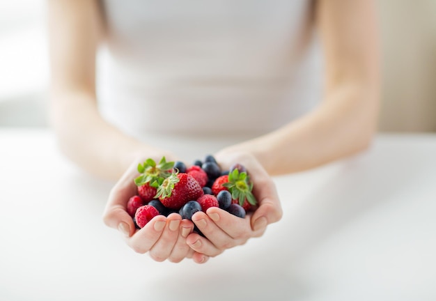 healthy eating, dieting, vegetarian food and people concept - close up of woman hands holding berries at home