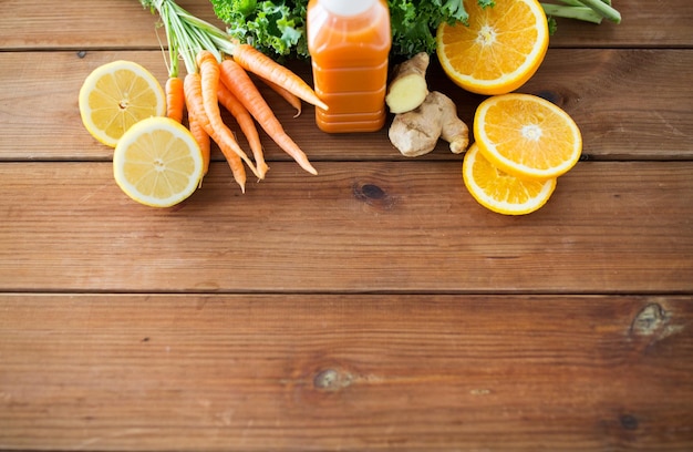 healthy eating, food, dieting and vegetarian concept - close up of bottle with carrot juice, fruits and vegetables on wooden table