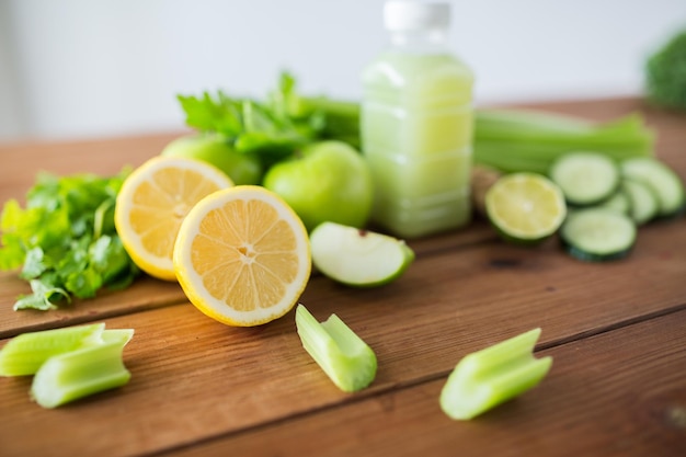 healthy eating, food, dieting and vegetarian concept - close up of bottle with green juice, fruits and vegetables on wooden table