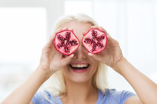 healthy eating, organic food, fruit diet, comic and people concept - happy woman having fun and covering her eyes with pomegranate